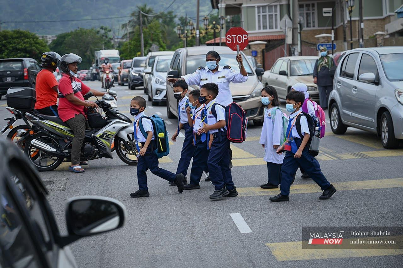 Beberapa murid melintas jalan sambil dibantu pengawal keselamatan di Sekolah Kebangsaan Taman Tasik, Ampang pada Mac lalu.