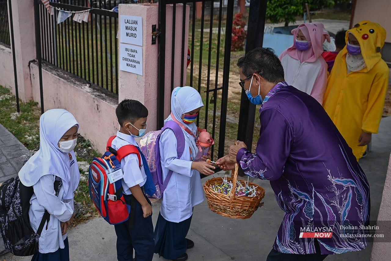 Seorang guru menyambut murid-murid Tahun Satu pada Mac lalu di Sekolah Kebangsaan Taman Tasik, Ampang.Guru dan kakitangan sekolah perlu divaksinasi untuk membolehkan sesi pembelajaran secara bersemuka diadakan di sekolah Oktober depan.