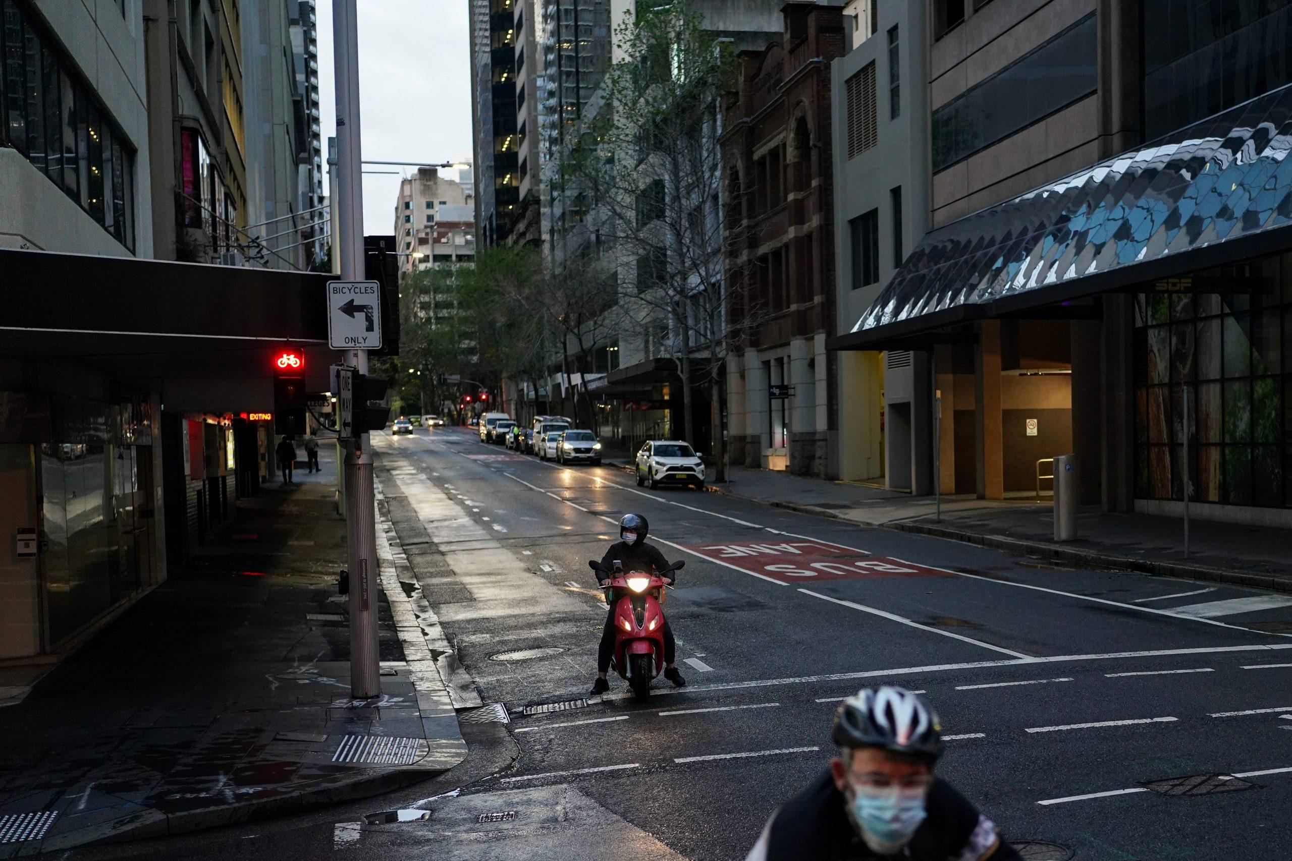 A delivery courier on a motorbike and a cyclist, both wearing protective face masks, navigate the city centre during a lockdown to curb the spread of the Covid-19 outbreak in Sydney, Australia, Sept 14. Photo: Reuters