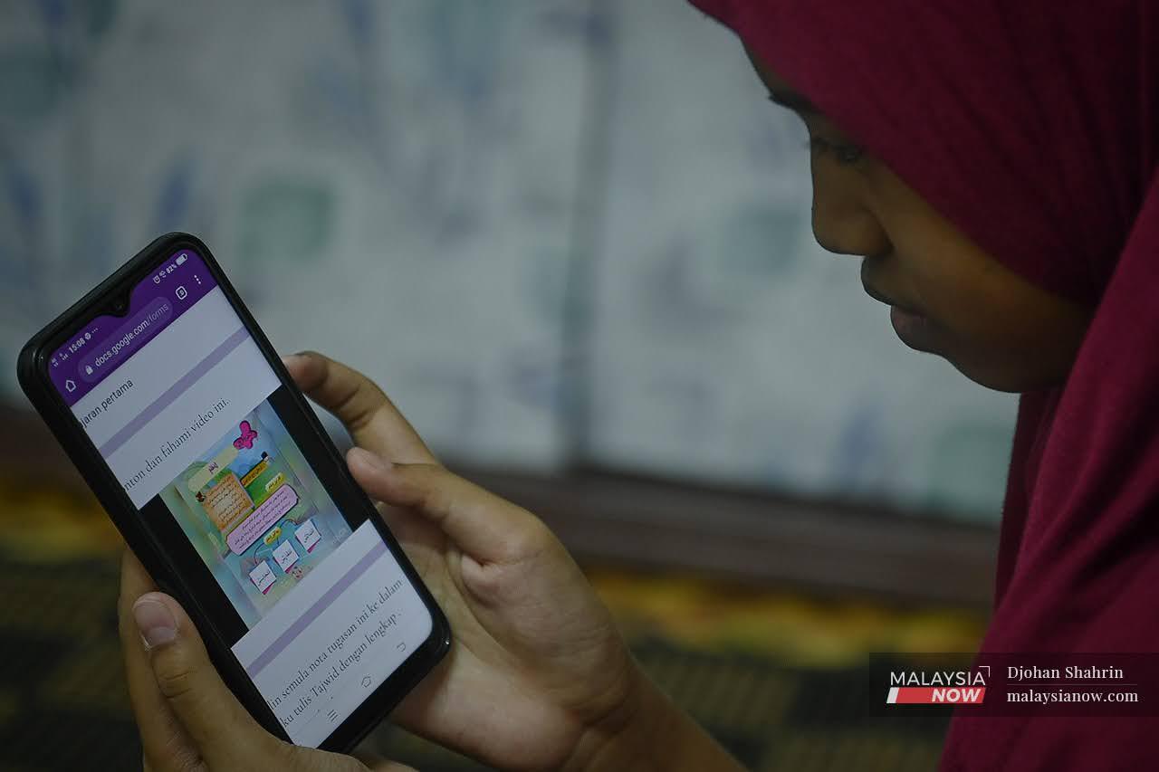Intan Nuramina Mohd Yunus, 12, menggunakan telefon bimbit ibunya untuk mengikuti pembelajaran dan pengajaran di rumah (PdPR) di Pangsapuri Taman Teknologi, Kajang. Pakej bantuan prabayar yang diumumkan KKMM hari ini bakal memberi manfaat kepada pelajar dan keluarga.