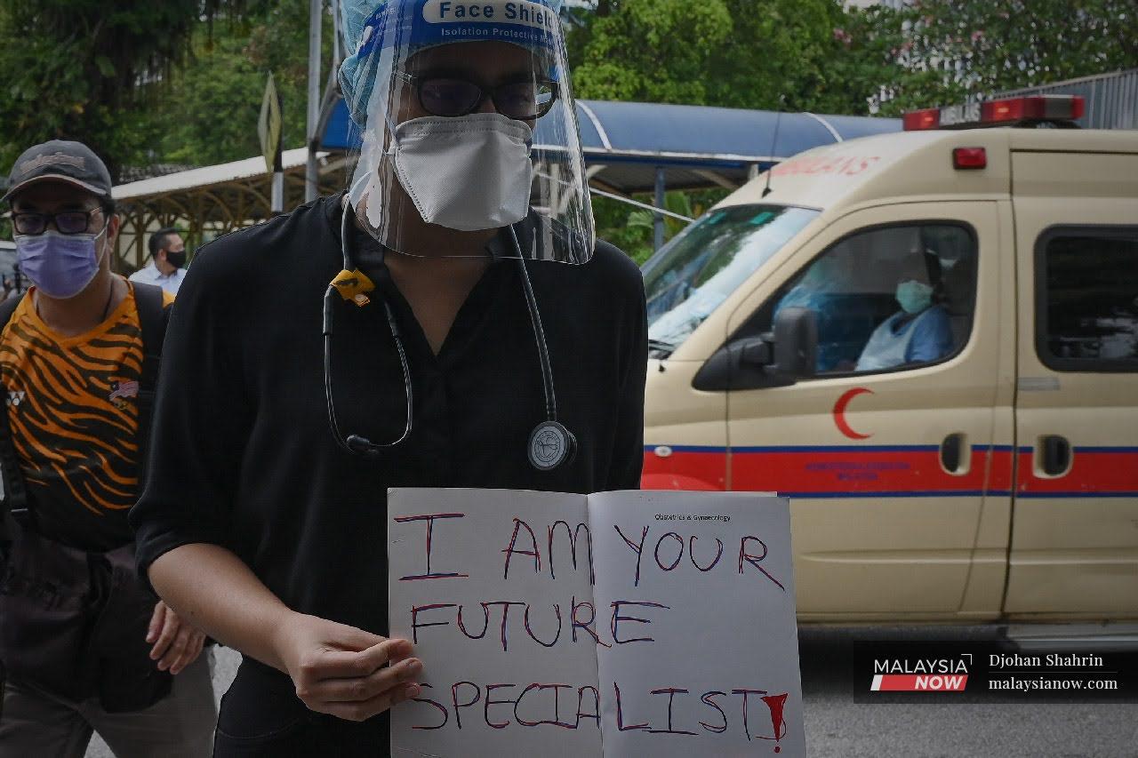 Seorang doktor kontrak berjalan keluar dari lobi utama sambil memegang plakad ketika mengadakan himpunan secara aman di Hospital Kuala Lumpur.