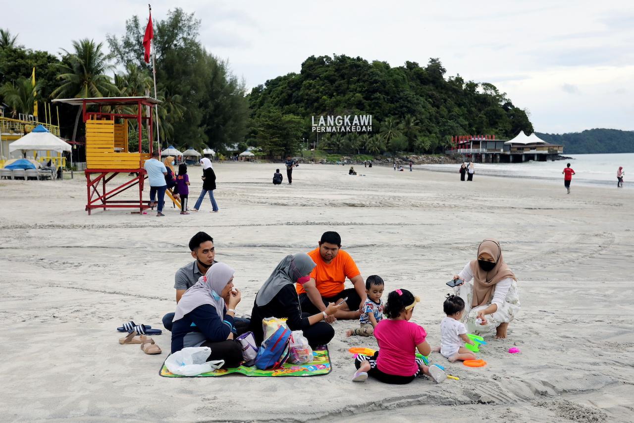 A family picnics by the sea while others stroll about at Pantai Cenang in Langkawi, which reopened to domestic tourists yesterday after months of lockdown due to Covid-19 restrictions. Photo: Reuters