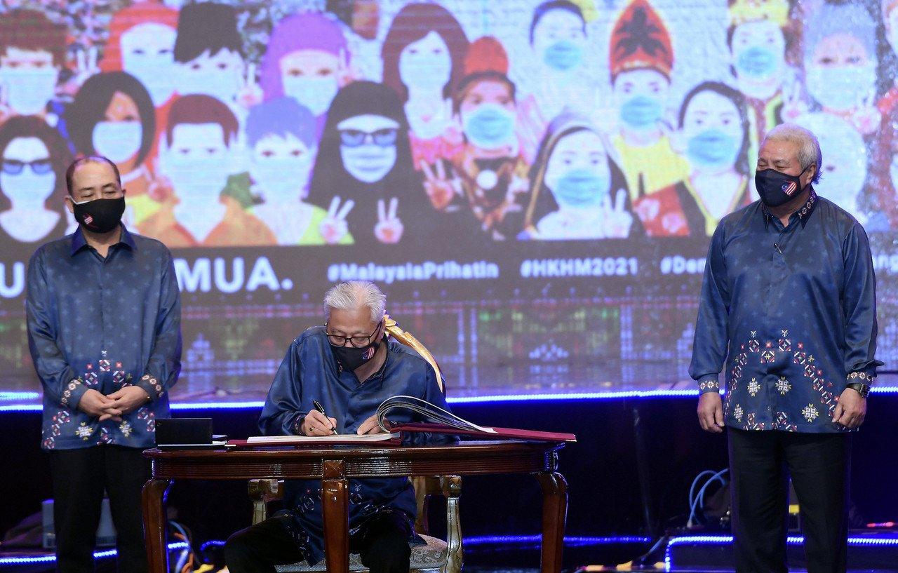 Perdana Menteri Ismail Sabri Yaakob menandatangani Buku Khas Sambutan Hari Malaysia Tahun 2021 di Pusat Konvensyen Antarabangsa Sabah (SICC) pada 16 September, 2021. Turut menyaksikan Ketua Menteri Sabah Hajiji Noor (kiri) dan Timbalan Ketua Menteri Sarawak Awang Tengah Ali Hasan (kanan). Gambar: Bernama