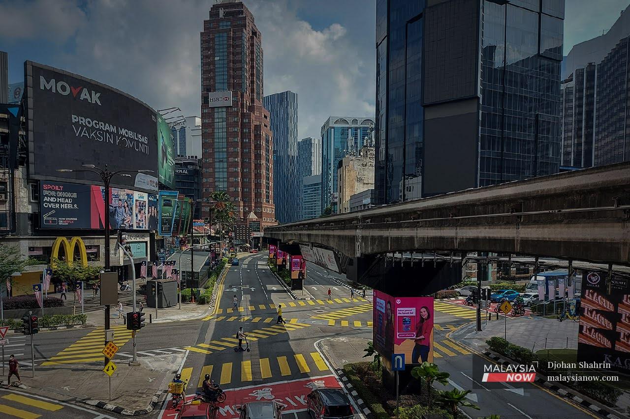 Pedestrians cross at the intersection of Jalan Sultan Ismail and Jalan Bukit Bintang in Kuala Lumpur beneath a billboard advertising the country's community mobile vaccination programme.