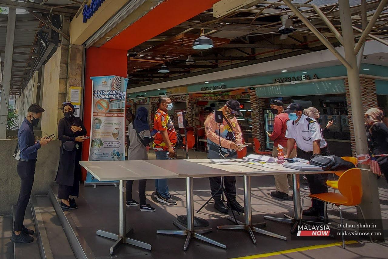 Customers queue to scan the QR code and show their MySejahtera status to the security guard on duty before entering a premise in Kuala Lumpur.