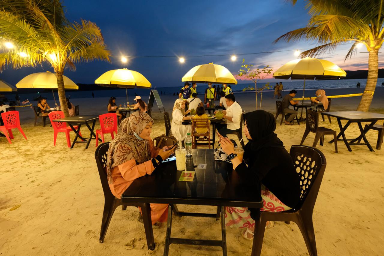 Diners enjoy a meal at Pantai Cenang in Langkawi as police monitor tourists' compliance with health SOPs. Photo: Bernama