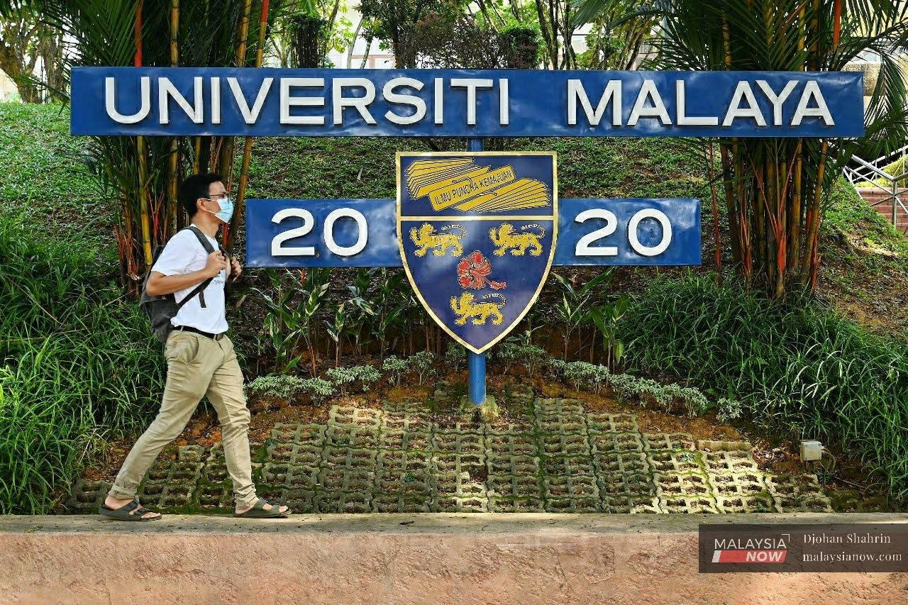 Pelajar Universiti Malaya berjalan di hadapan papan tanda universiti dengan memakai pelitup muka.