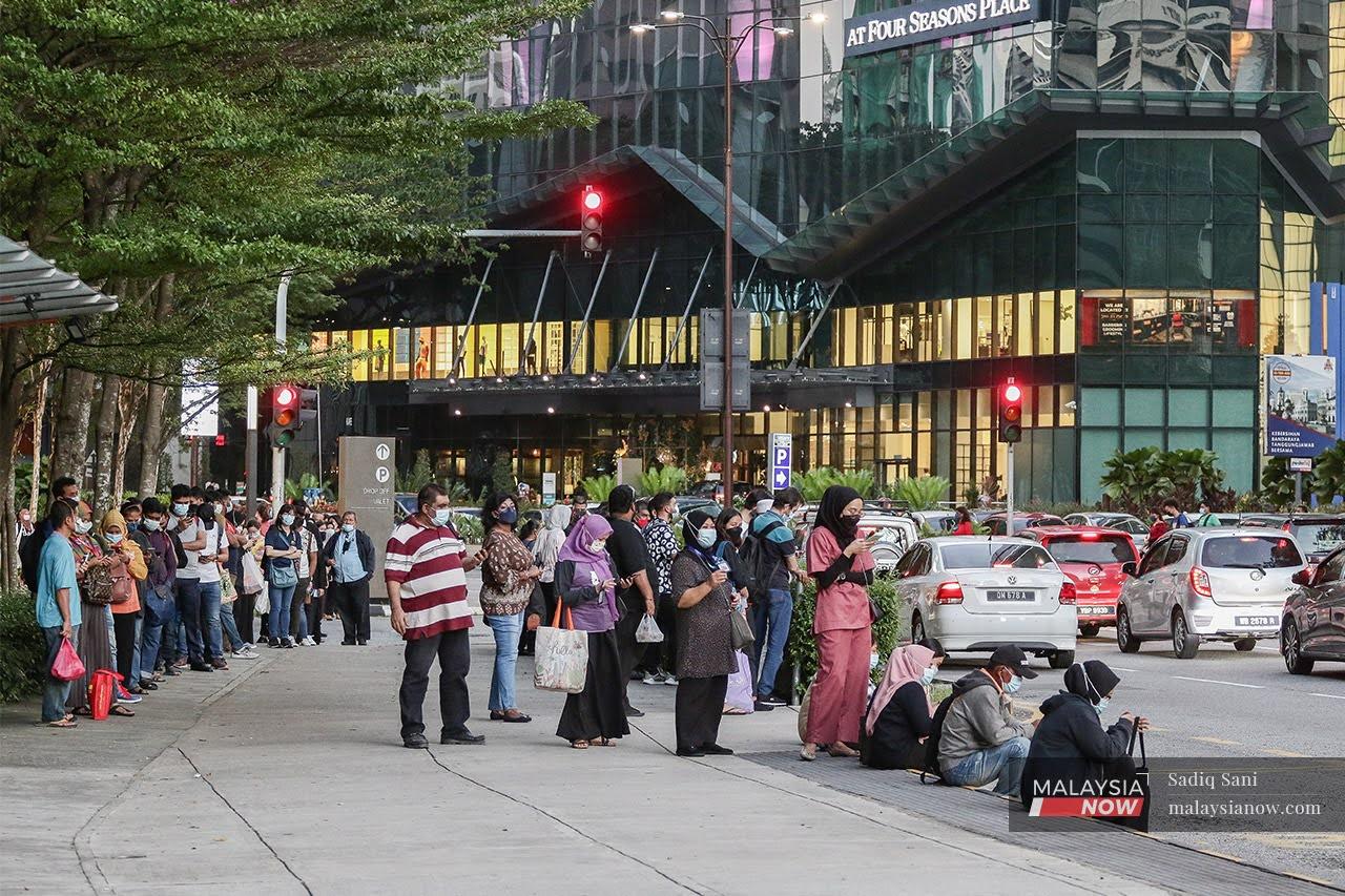 Commuters wearing face masks wait for the bus after office hours at Jalan Ampang in Kuala Lumpur.