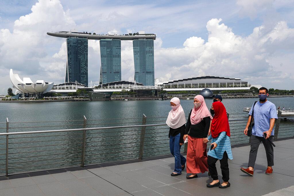 People, wearing face masks,  walk on a bridge along the Marina Bay area in Singapore, Tuesday, June 30, 2020. (AP Photo/Yong Teck Lim)