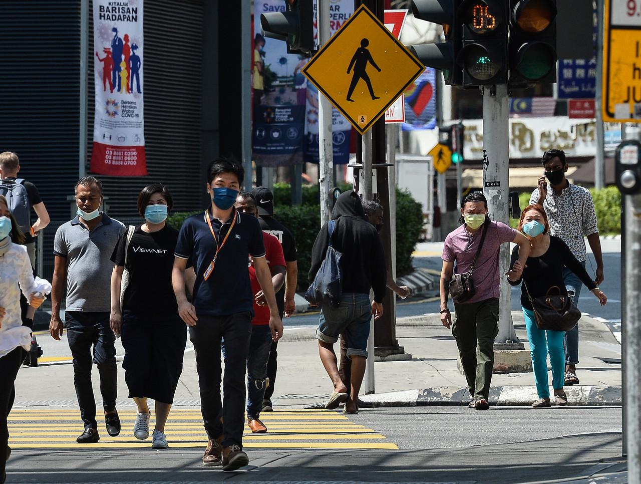 Pedestrians wearing face masks cross a road in Kuala Lumpur today. Photo: Bernama