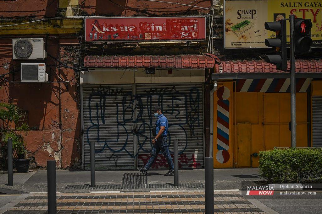 A man walks past a row of shops in Kuala Lumpur closed under the movement control order.