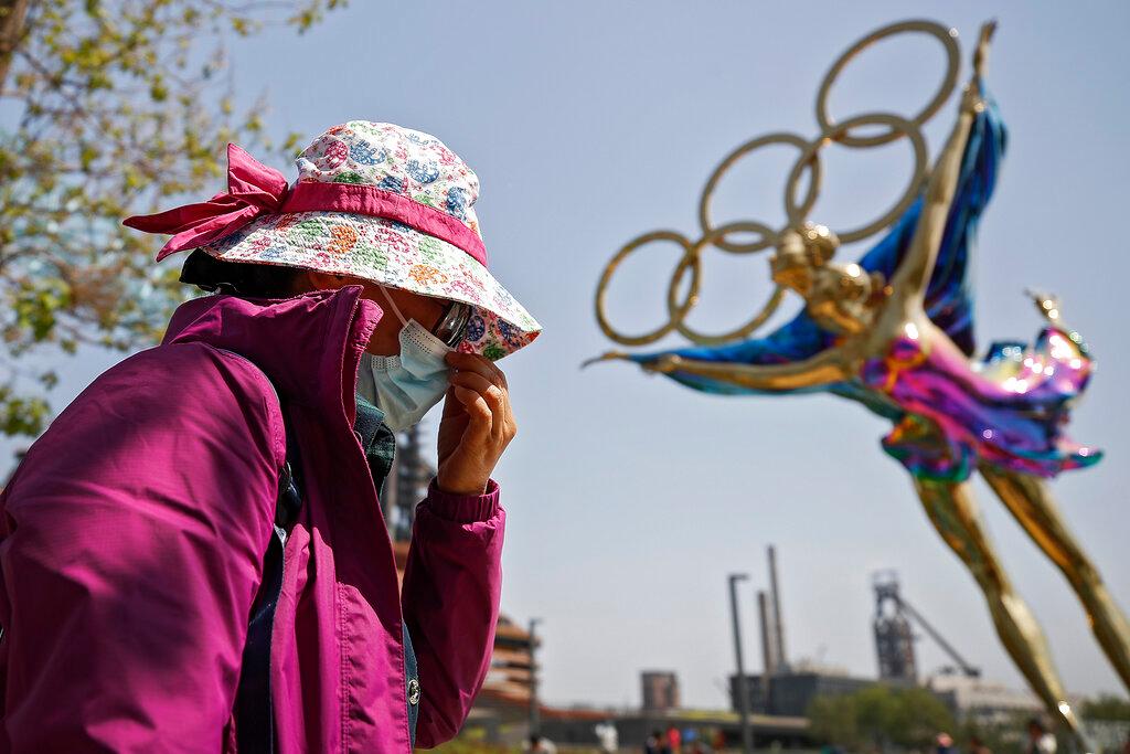 A woman adjusts her face mask as she walks by a statue featuring the Beijing Winter Olympics figure skating on display at the Shougang Park in Beijing in this May 2 file photo. Photo: AP