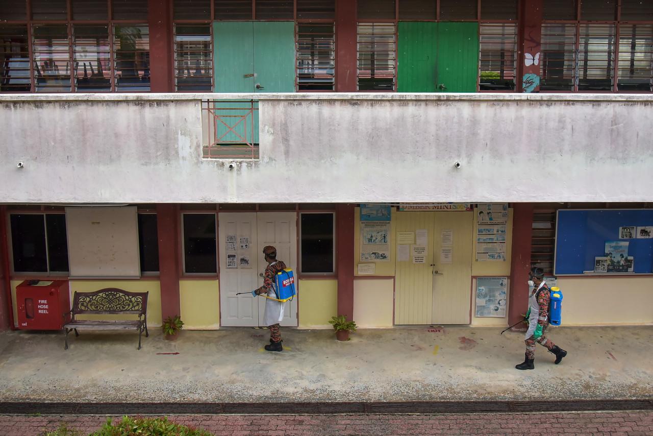 Staff from the fire and rescue department wearing personal protective equipment spray disinfectant at a secondary school in Labuan today, ahead of the reopening of school sessions on Oct 4. Photo: Bernama