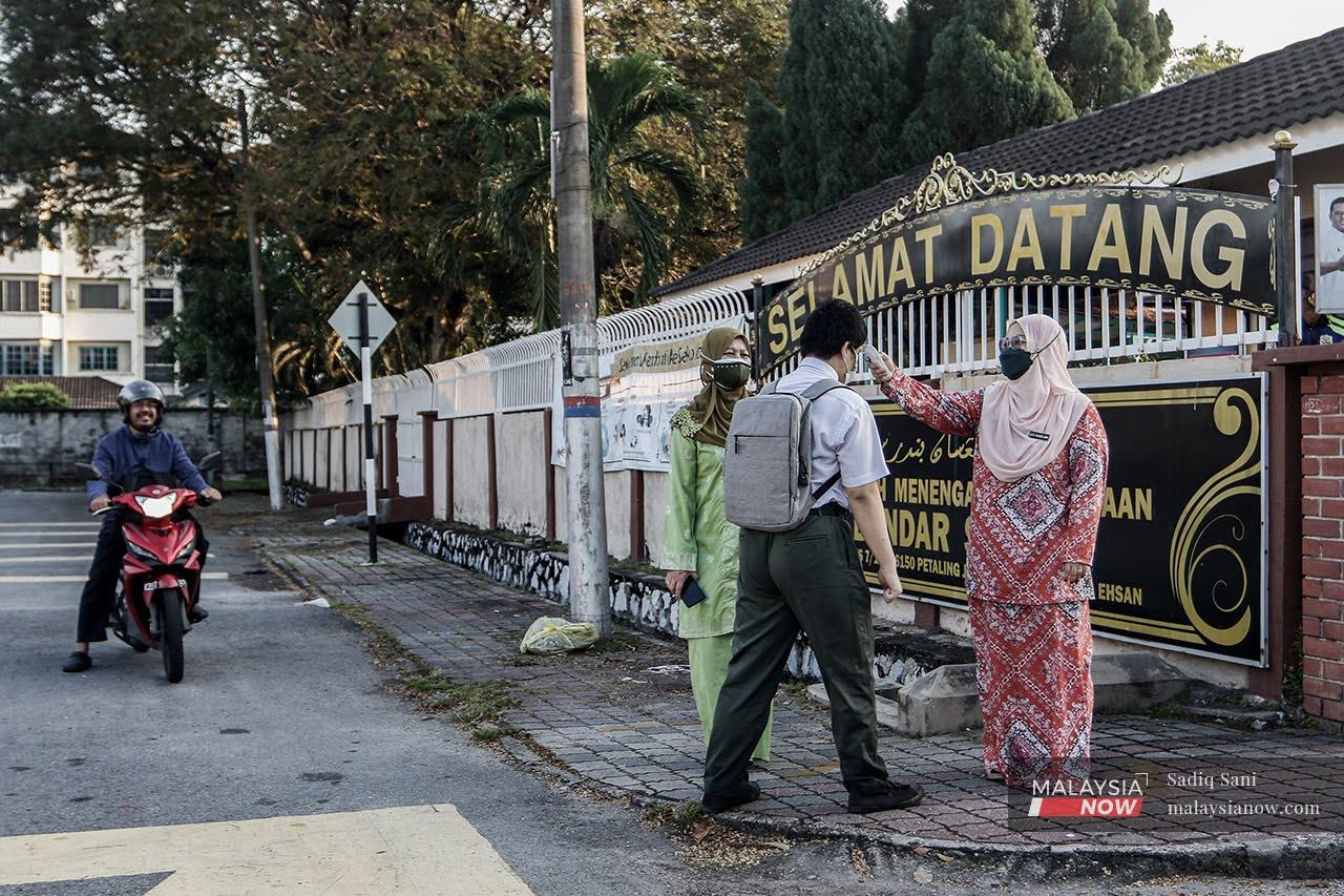 A teacher takes a student's temperature at the main entrance of SMK Bandar Sunway in Petaling Jaya, as schools in the Klang Valley reopen for face-to-face classes.