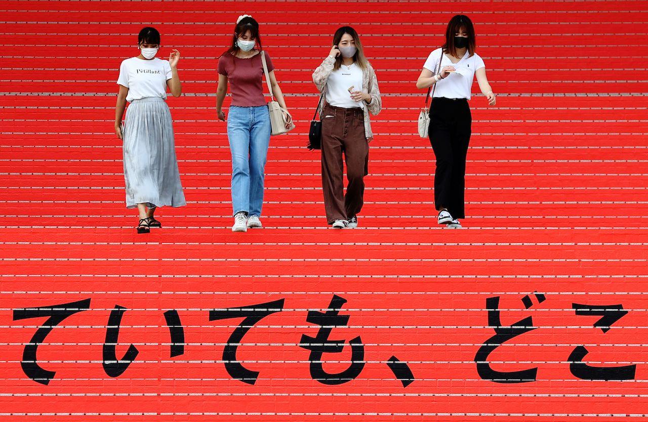 Women wearing protective masks walk down a flight of stairs bearing a slogan cheering on the Japanese team during Tokyo 2020 Olympic Games in Tokyo, Japan, Aug 7. Photo: Reuters