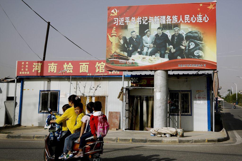An Uighur woman and her children ride past a picture of China's President Xi Jinping joining hands with a group of Uighur elders at the Unity New Village in Hotan, in western China's Xinjiang region, Sept 20, 2018. Photo: AP