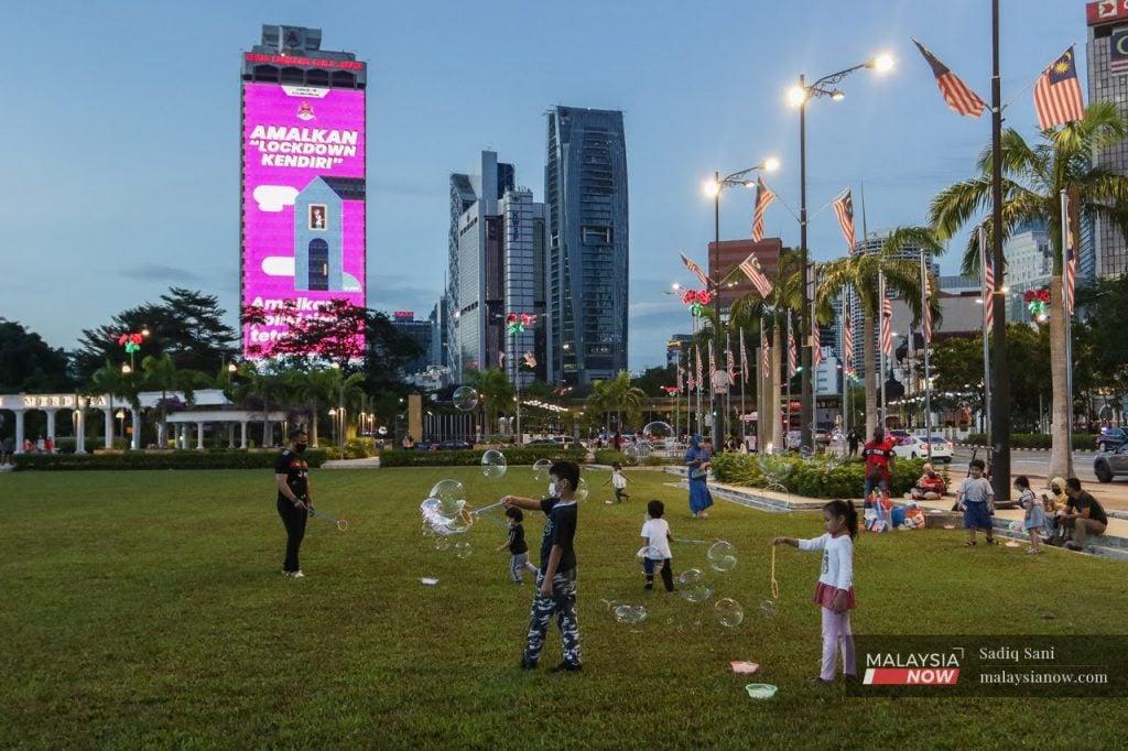 Children blow bubbles at Dataran Merdeka in Kuala Lumpur while a nearby billboard reminds the public to continue adhering to health SOPs. Chief statistician Mohd Uzir Mahidin says the birth rate was already on the decline before Covid-19 but that the pandemic may have contributed to the drop.