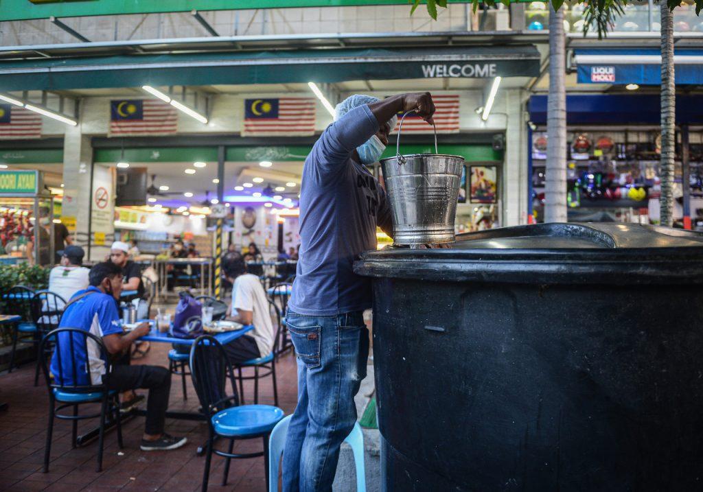 Seorang pekerja restoran di Sentul, Kuala Lumpur mengambil air daripada tadahan ketika bekalan air terganggu pada 13 Oktober. Gambar: Bernama