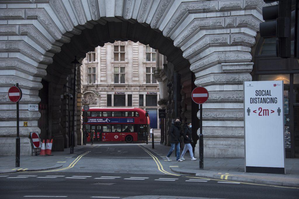 People wear face masks as they walk past a social distancing sign in Regent Street, in London, Jan 9, during England's third national lockdown to curb the spread of coronavirus. Photo: AP