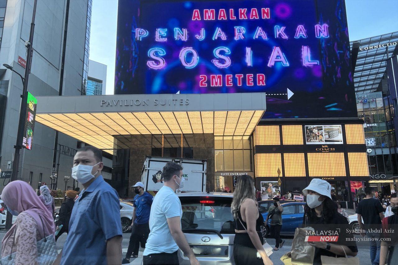 Pedestrians cross a road in Bukit Bintang, Kuala Lumpur, below a huge billboard reminding people to maintain a safe distance from each other to curb the spread of Covid-19.