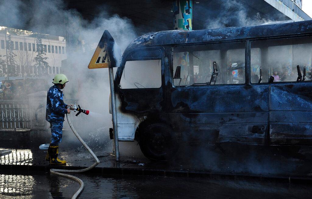 In this photo released by the Syrian official news agency Sana, a Syrian firefighter extinguishes a burned bus at the site of a deadly explosion, in Damascus, Syria, Oct 20. Photo: AP