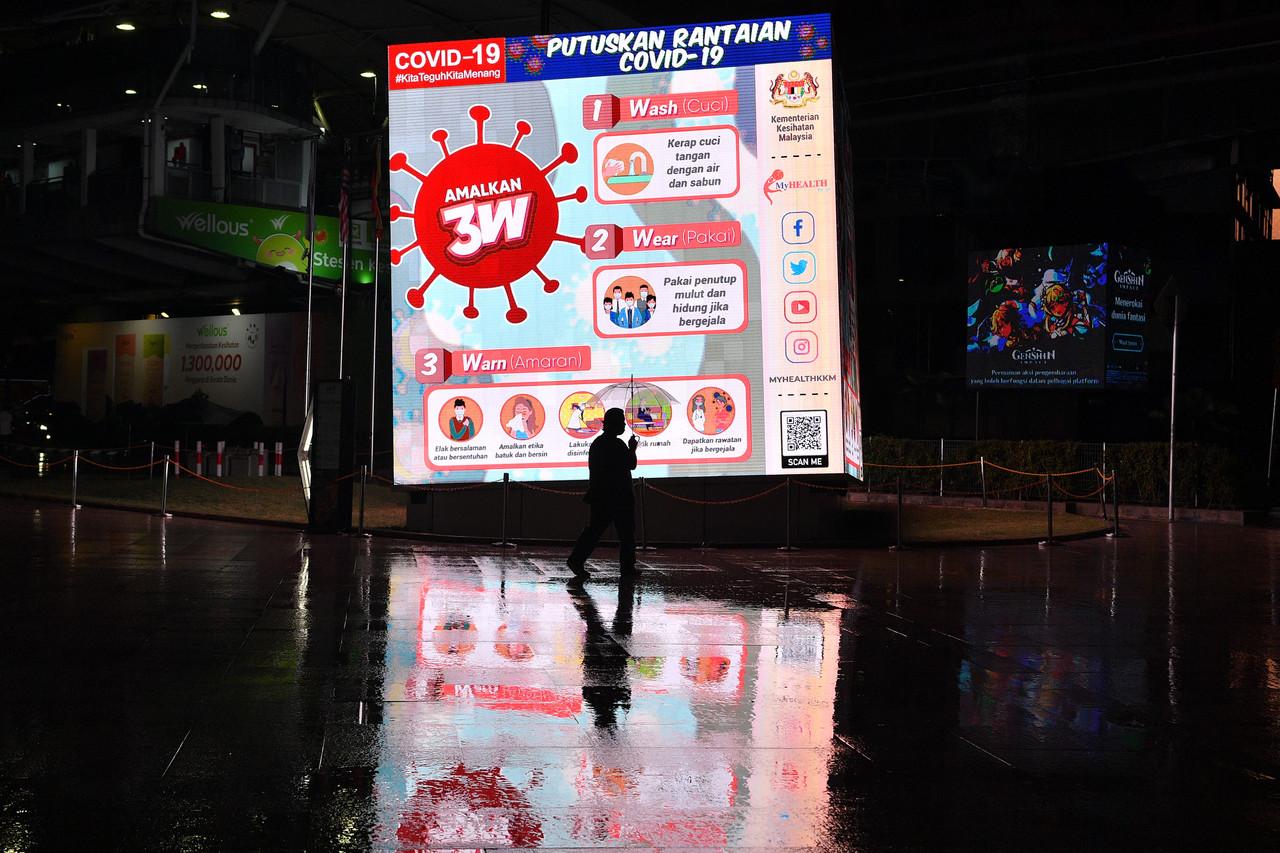 A man holding an umbrella walks past a giant digital billboard in Kuala Lumpur reminding the public to adhere to Covid-19 SOPs. Photo: Bernama