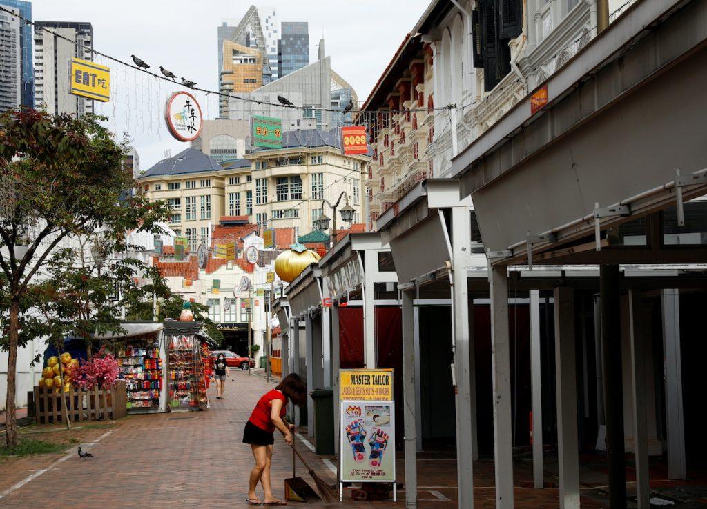 A woman sweeps the floor near closed down shops in the largely empty Chinatown tourist district in Singapore, Aug 30. Photo: Reuters