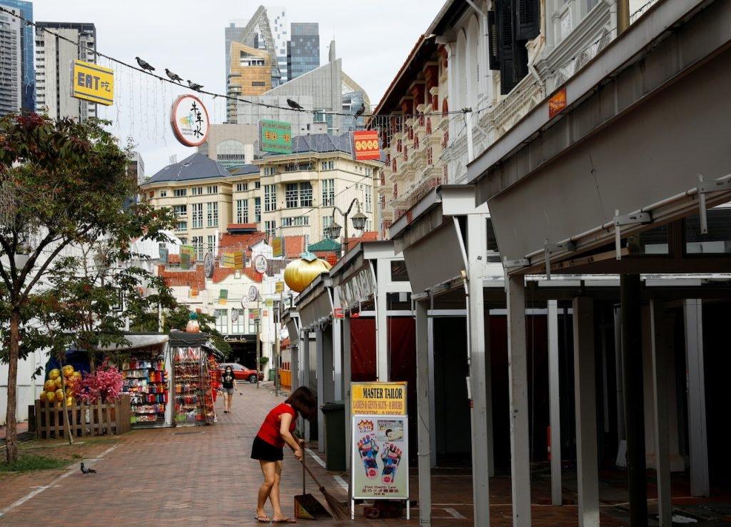 Seorang wanita menyapu bahagian luar premis perniagaan yang kini ditutup ekoran lanjutan sekatan aktiviti sosial bagi membendung wabak Covid-19 yang melonjak secara  mendadak di Singapura. Gambar: Reuters