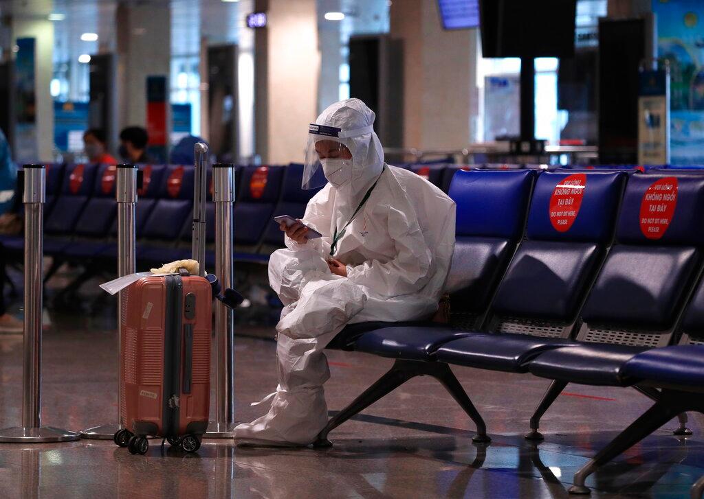 A passenger in a full protective suit uses a phone while waiting to board a flight at Tan Son Nhat airport in Ho Chi Minh city, Vietnam, Oct 15. Photo: AP