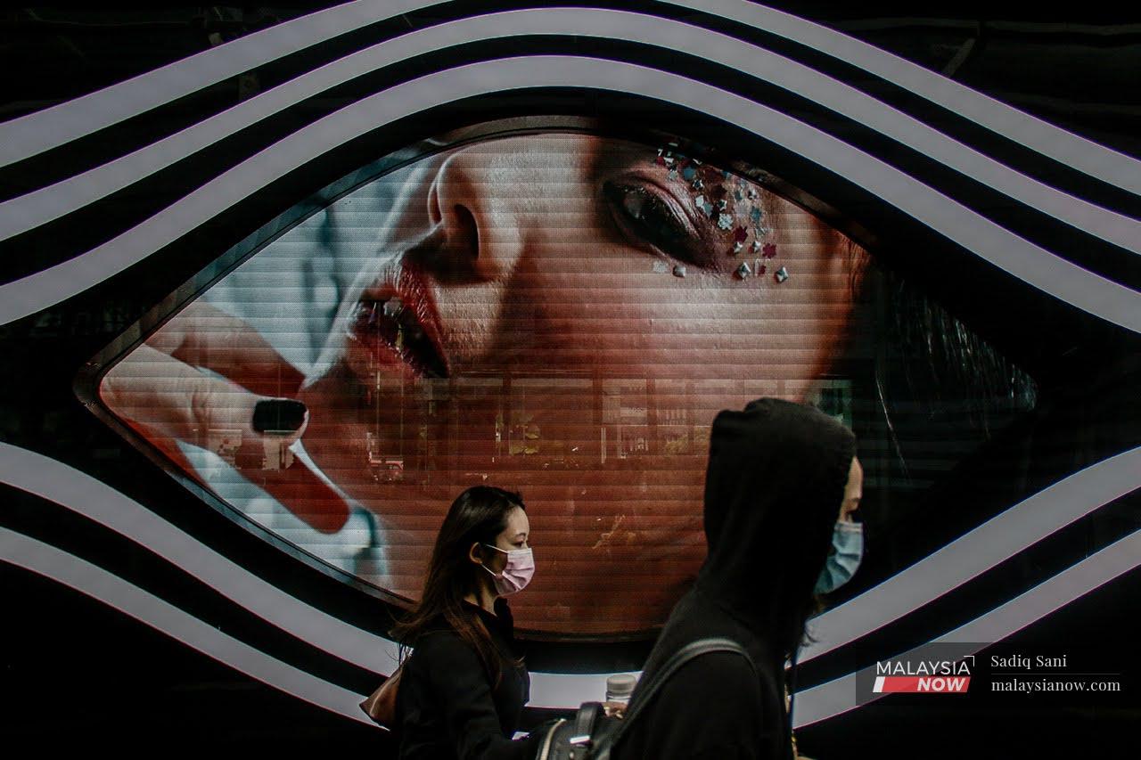 Women wearing face masks walk past a digital billboard in the shopping district of Bukit Bintang in Kuala Lumpur.
