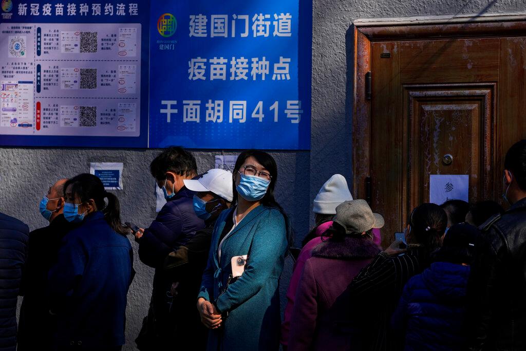 A woman wearing a face mask to help curb the spread of the coronavirus looks back as she lines up with masked residents to receive booster shots against Covid-19 at a vaccination site near a residential area in Beijing, Oct 22. Photo: AP