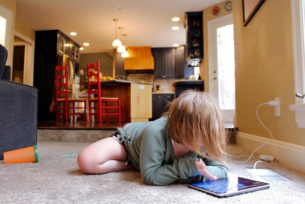 A young girl sprawls on the floor to play games on an iPad in this file picture dated Oct 30, 2020. Photo: AP
