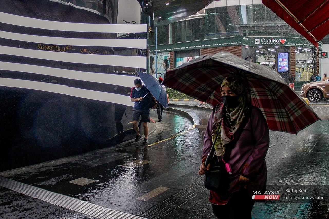 Orang ramai memakai pelitup muka berjalan meranduk hujan di ibu negara Kuala Lumpur.