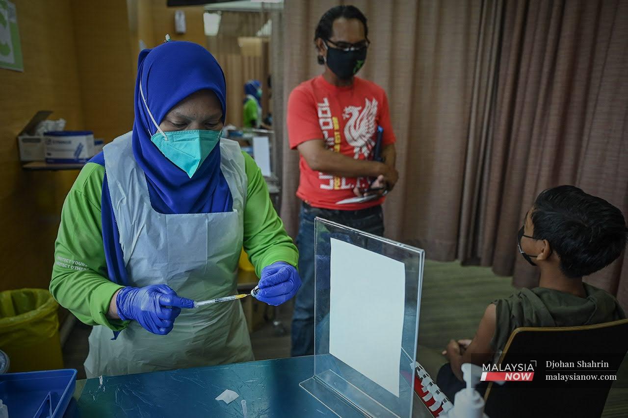 Petugas kesihatan membuat persediaan sebelum memberi suntikan vaksin Pfizer kepada Azrif Arfan Cama Adrian yang berusia 12 tahun di Pusat Pemberian Vaksin KPJ Tawakkal, Jalan Pahang.