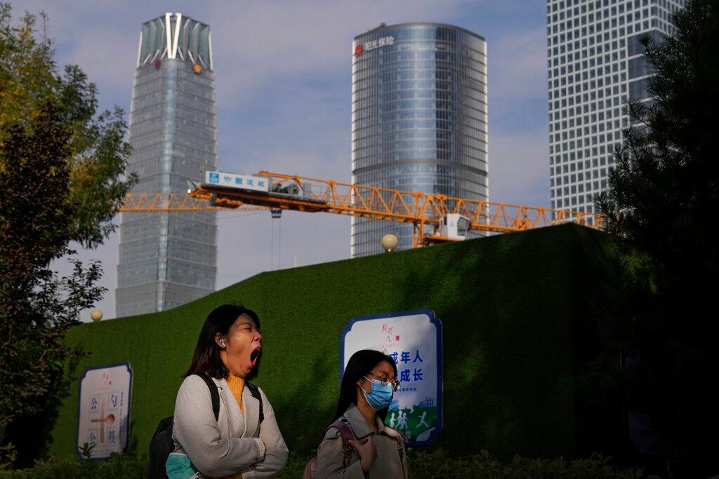 A woman holding a face mask yawns while passing by a construction crane at the Central Business District in Beijing, Oct 18. While China acknowledges that high-rise buildings promote intensive use of land resources, it is increasingly concerned that local officials are blindly pursuing construction with little attention to practicality and safety. Photo: AP