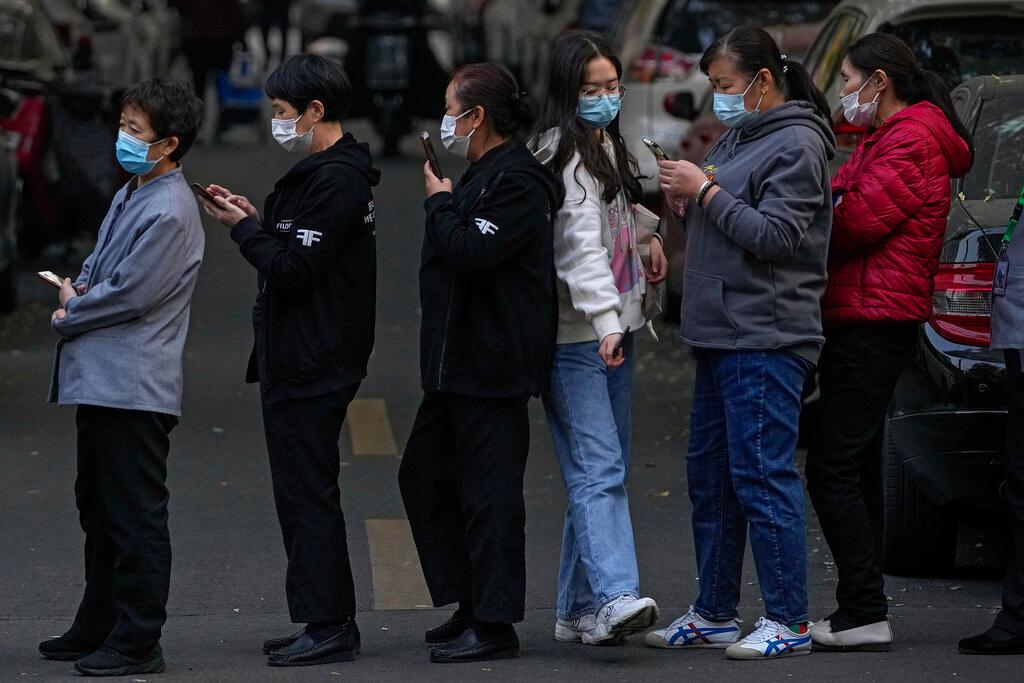 A woman wearing a face mask to help curb the spread of the coronavirus walks through a line of masked service sector women waiting to receive a swab for Covid-19 tests during a mass testing in Beijing, Oct 29, following a spike of the coronavirus in the capital and other provincials. Photo: AP