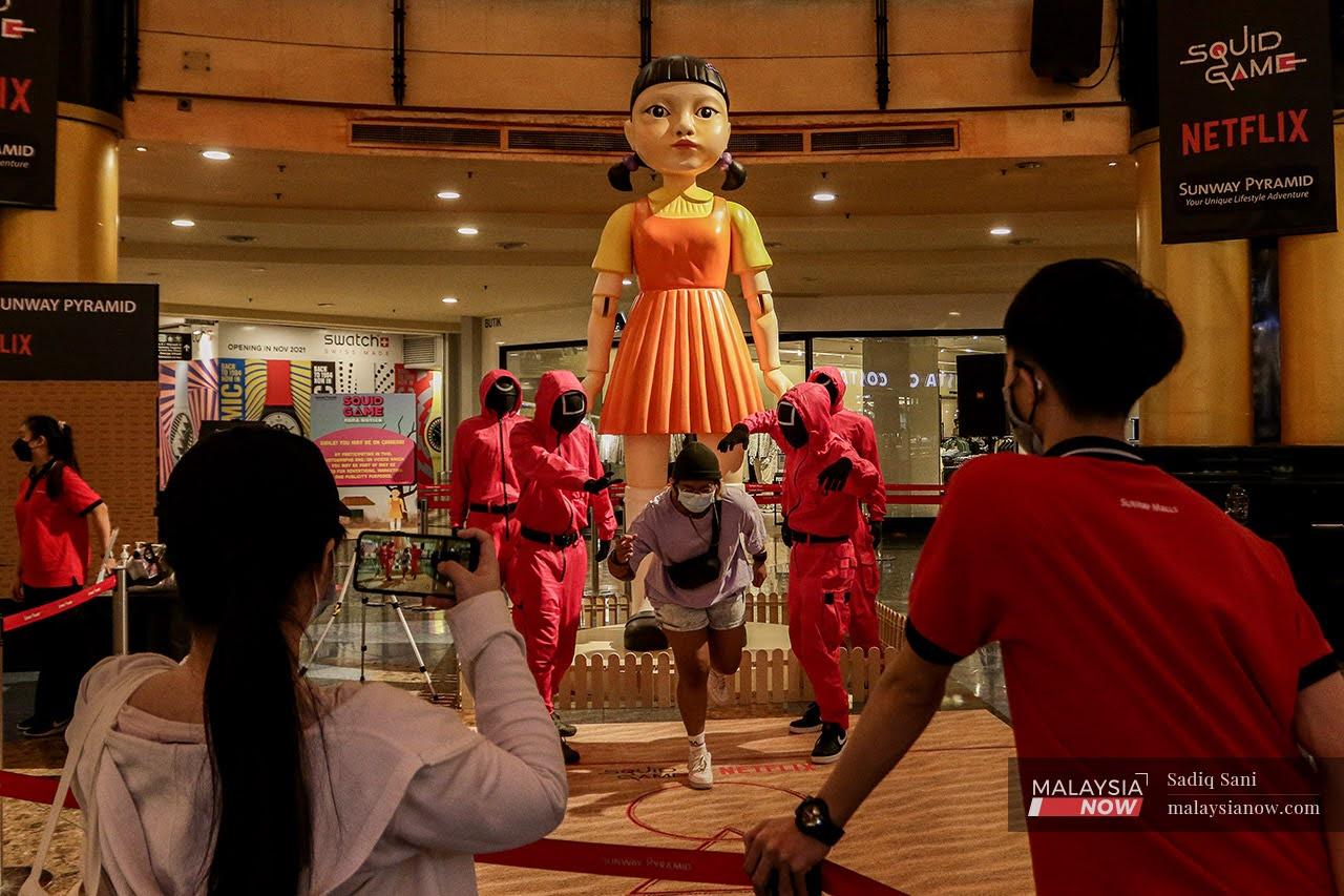 A girl poses for a picture with cosplayers dressed up as characters from Netflix show 'Squid Game' at a shopping mall in Subang Jaya, Selangor.