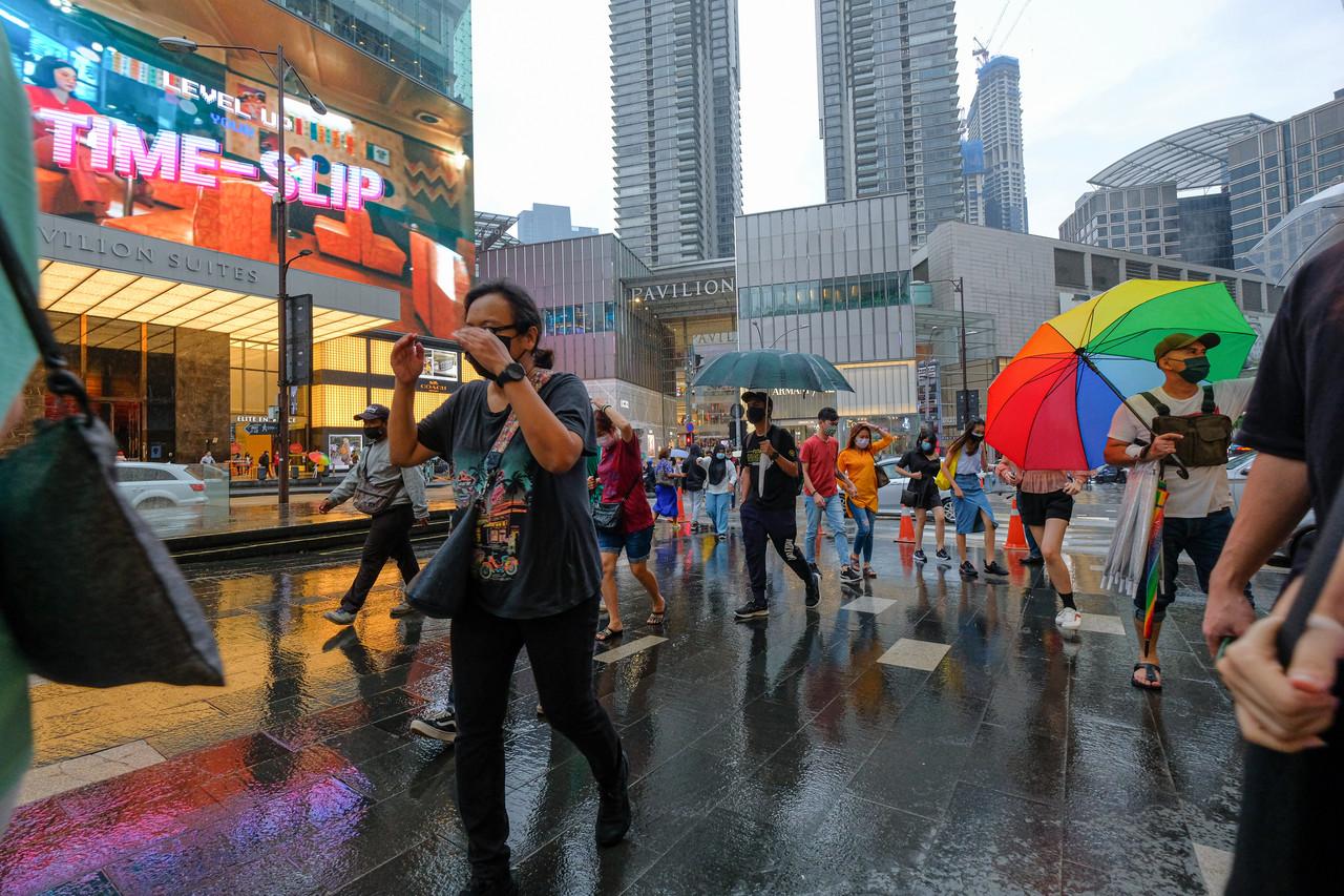 Pedestrians shield themselves from the rain as they make their way through Bukit Bintang in Kuala Lumpur. Photo: Bernama