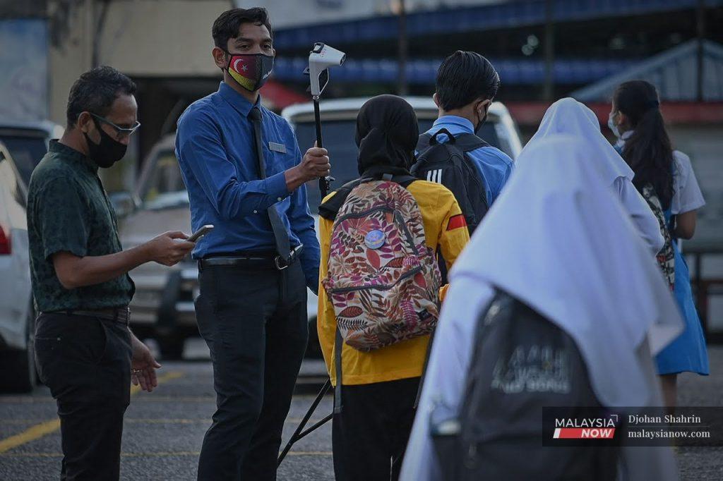 A teacher at a school im Ampang, Selangor, holds up a thermometer for students to check their temperatures as they return for face-to-face classes under Phase Four of the National Recovery Plan.