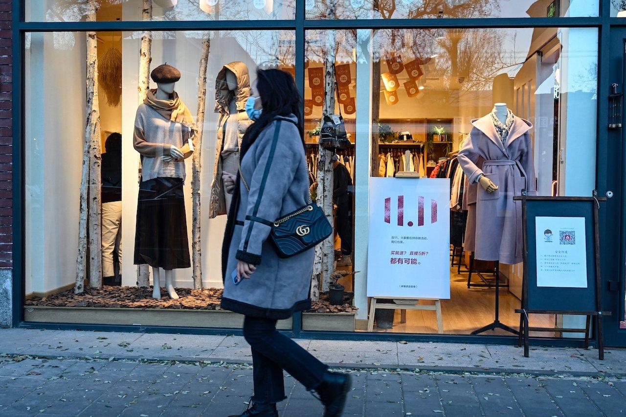 A woman walks past a clothing store with a poster promoting the annual 'Singles’ Day' on Nov 11, the biggest shopping day of the year, along a street in Beijing on Nov 10. Photo: AFP
