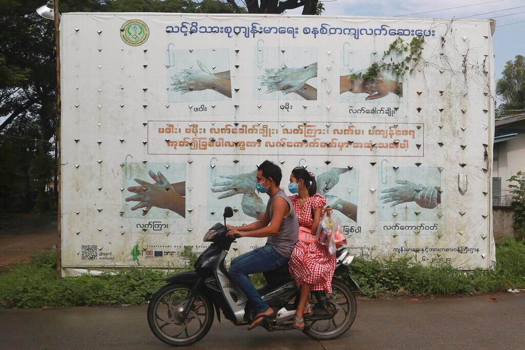 People wearing face masks to help curb the spread of the coronavirus ride a motorcycle past a health ministry public information campaign billboard about proper hand washing in Shwe Pyi Thar township in Yangon, Myanmar, July 28. Photo: AP