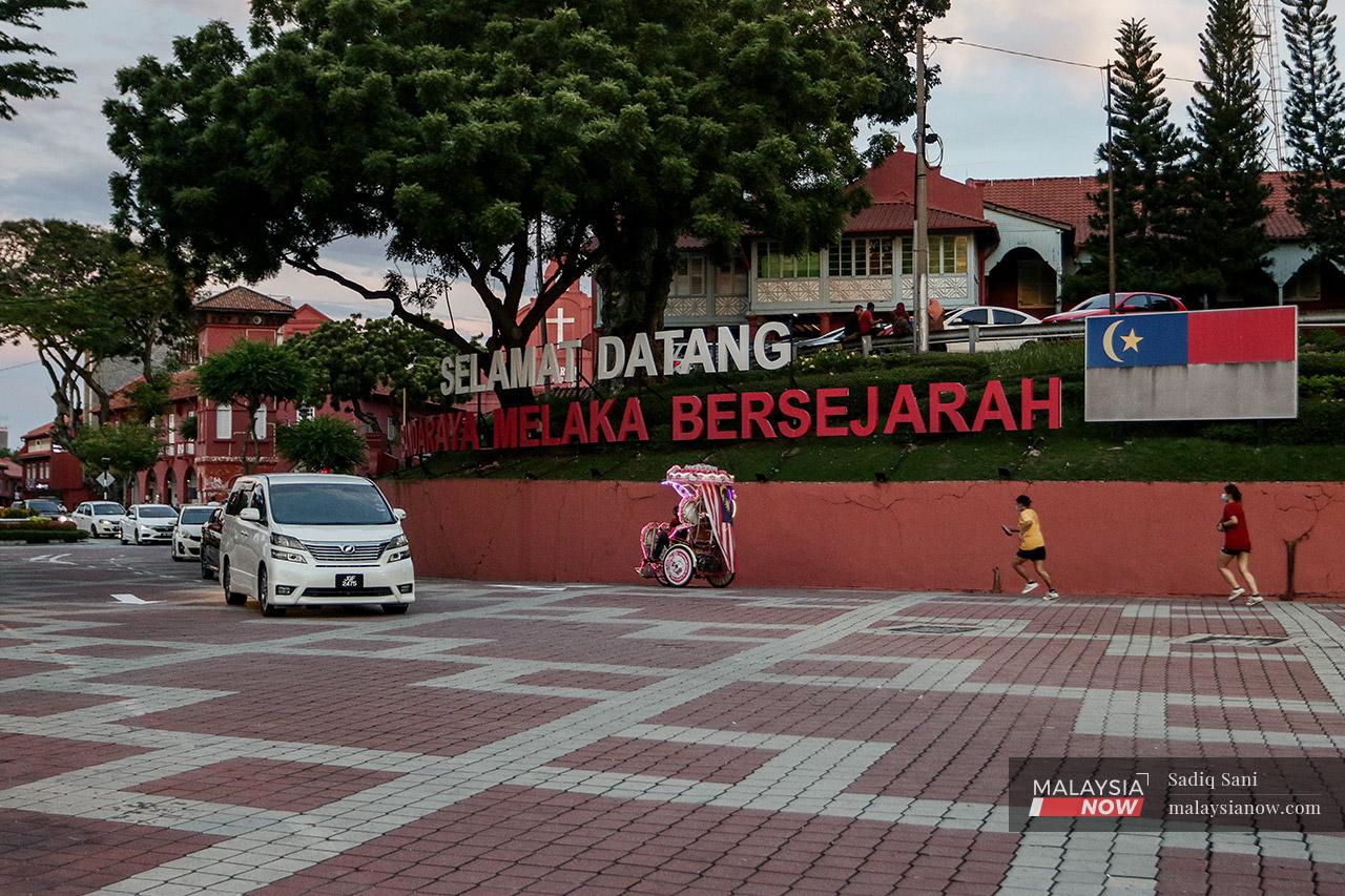 Joggers run behind a trishaw man beneath a billboard near the iconic Christ Church, welcoming visitors to the historic state of Melaka which will go to the polls to decide on a new administration on Nov 20.