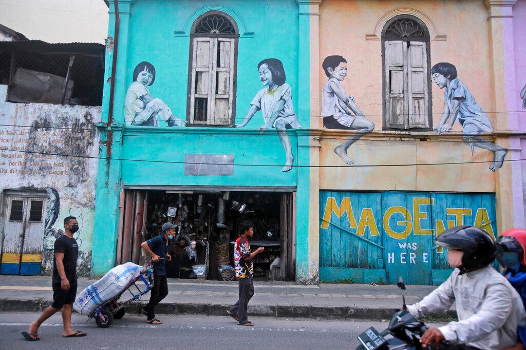 People walk past the facade of a building adorned with murals depicting playing children, in Medan, North Sumatra, Indonesia, Nov 1. Indonesia's Ulama Council has likened crypto to gambling, which is haram or forbidden under Islamic law. Photo: AP