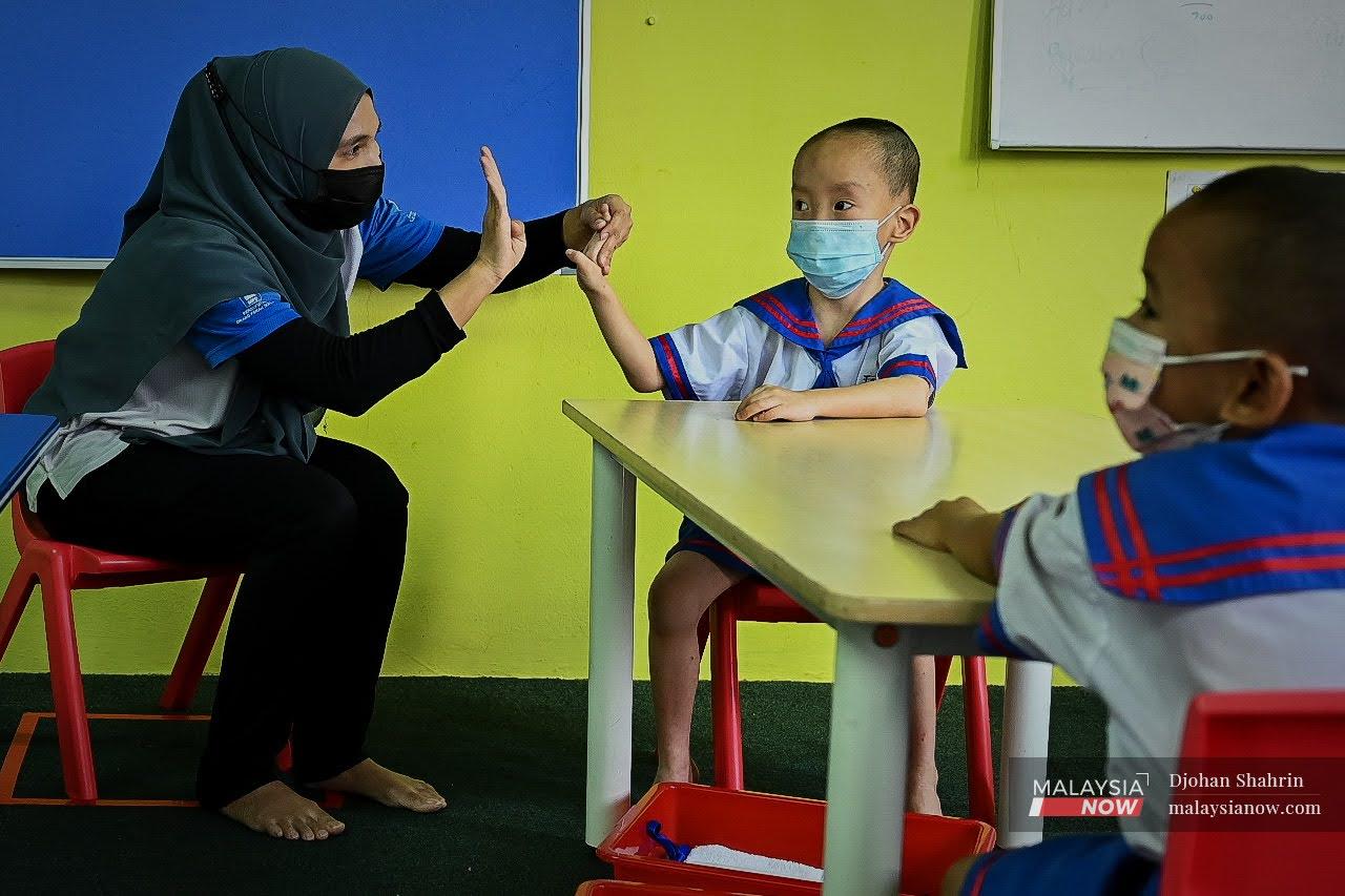Guru memperbetulkan isyarat pada tangan muridnya ketika mempelajari kemahiran bahasa isyarat.