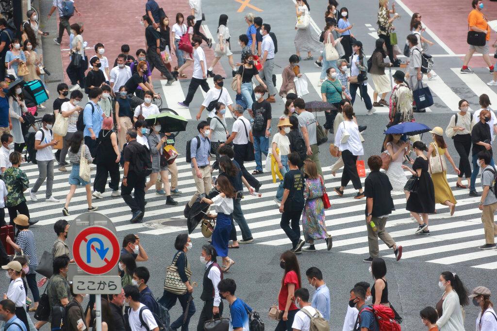 People wearing face masks to protect against the spread of the coronavirus cross a street in Tokyo, July 28. Japan has weathered the pandemic better than many countries, with just over 18,000 deaths so far and without the imposition of stringent lockdowns. Photo: AP