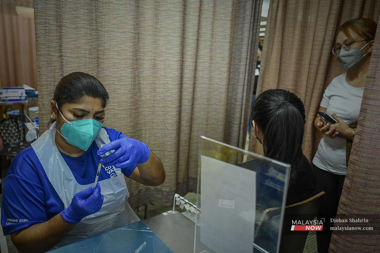 Petugas kesihatan membuat persediaan sebelum memberi suntikan vaksin Pfizer Bio-NTech kepada Roffina Marilyn Bredye Sodusta, 13 yang ditemani ibunya  di Pusat Pemberian Vaksin KPJ Tawakkal, Jalan Pahang.