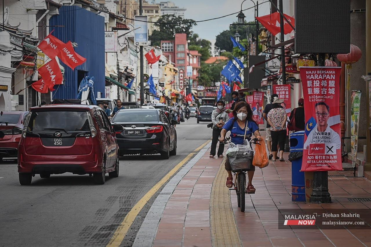 Penunggang basikal melalui deretan kain rentang calon PRN yang dipasang di Jonker Street. Pengundi disarankan membuat ujian kendiri sebelum pulang mengundi di Melaka.