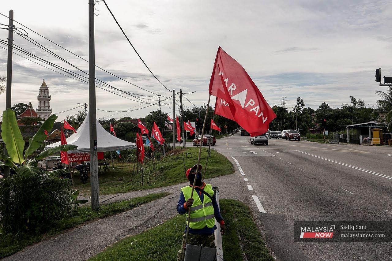 An election worker puts up Pakatan Harapan flags along the junction of Jalan Tanjung Kling in Melaka ahead of the state election this weekend.