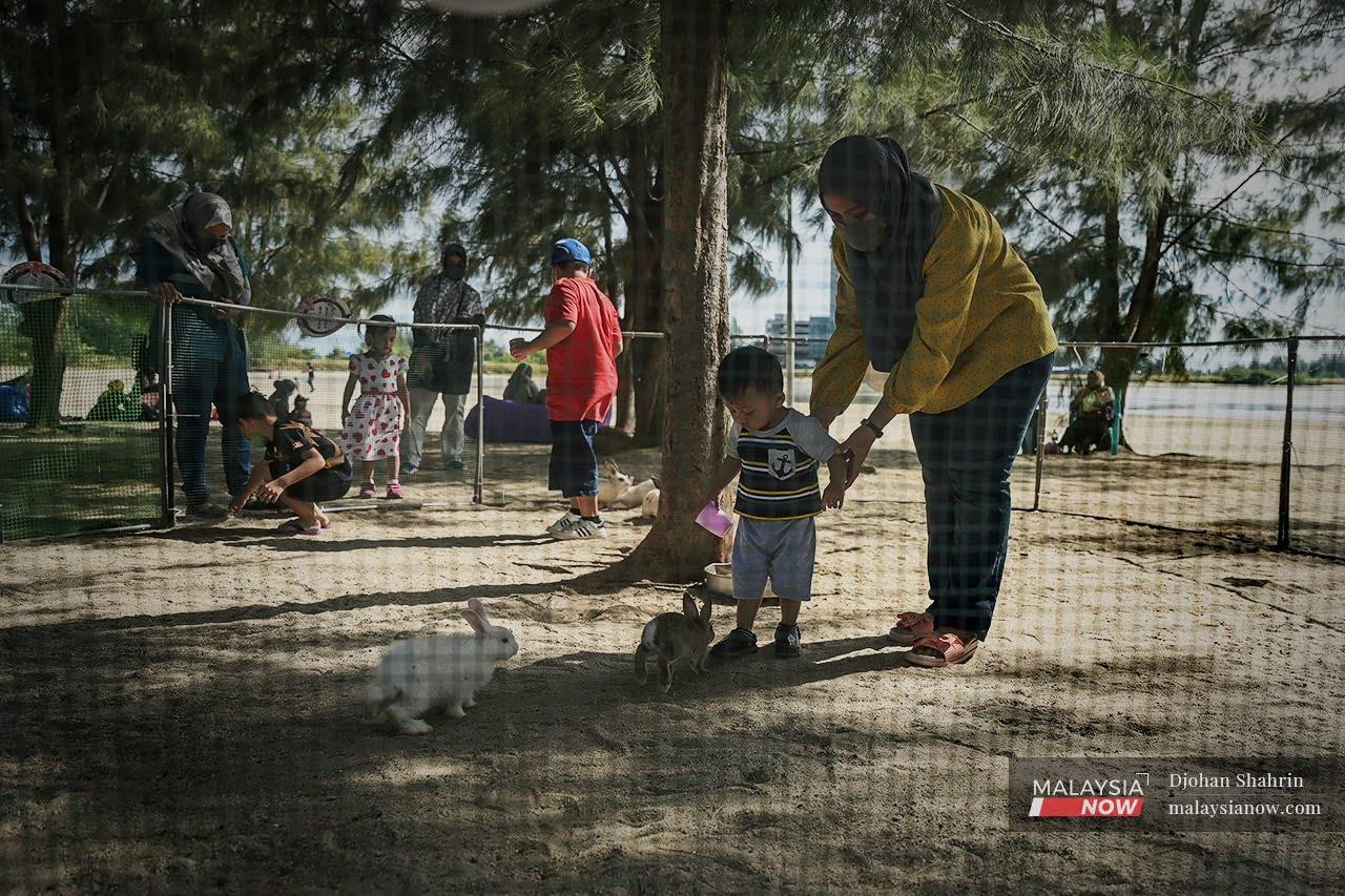 Seorang kanak-kanak ditemani ibunya bermain dengan arnab di Pantai Klebang, Melaka. Orang ramai menikmati kelonggaran selepas kadar vaksinasi semakin meningkat di bawah PICK.