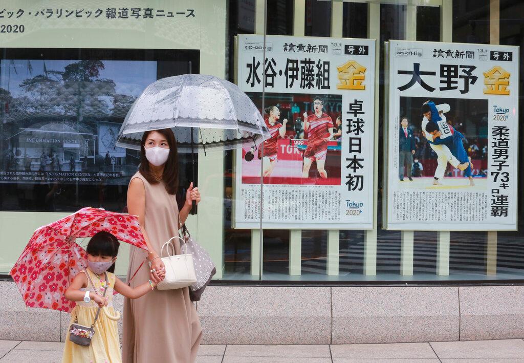 People wearing face masks to protect against the spread of the Covid-19 walk past extra papers reporting on Japanese gold medalists at Tokyo Olympics, in Tokyo, July 27. The stimulus package comes after Japan's economy shrank far more than expected in the second quarter as leaders struggled to overcome virus surges by imposing containment measures in Tokyo and other cities. Photo: AP